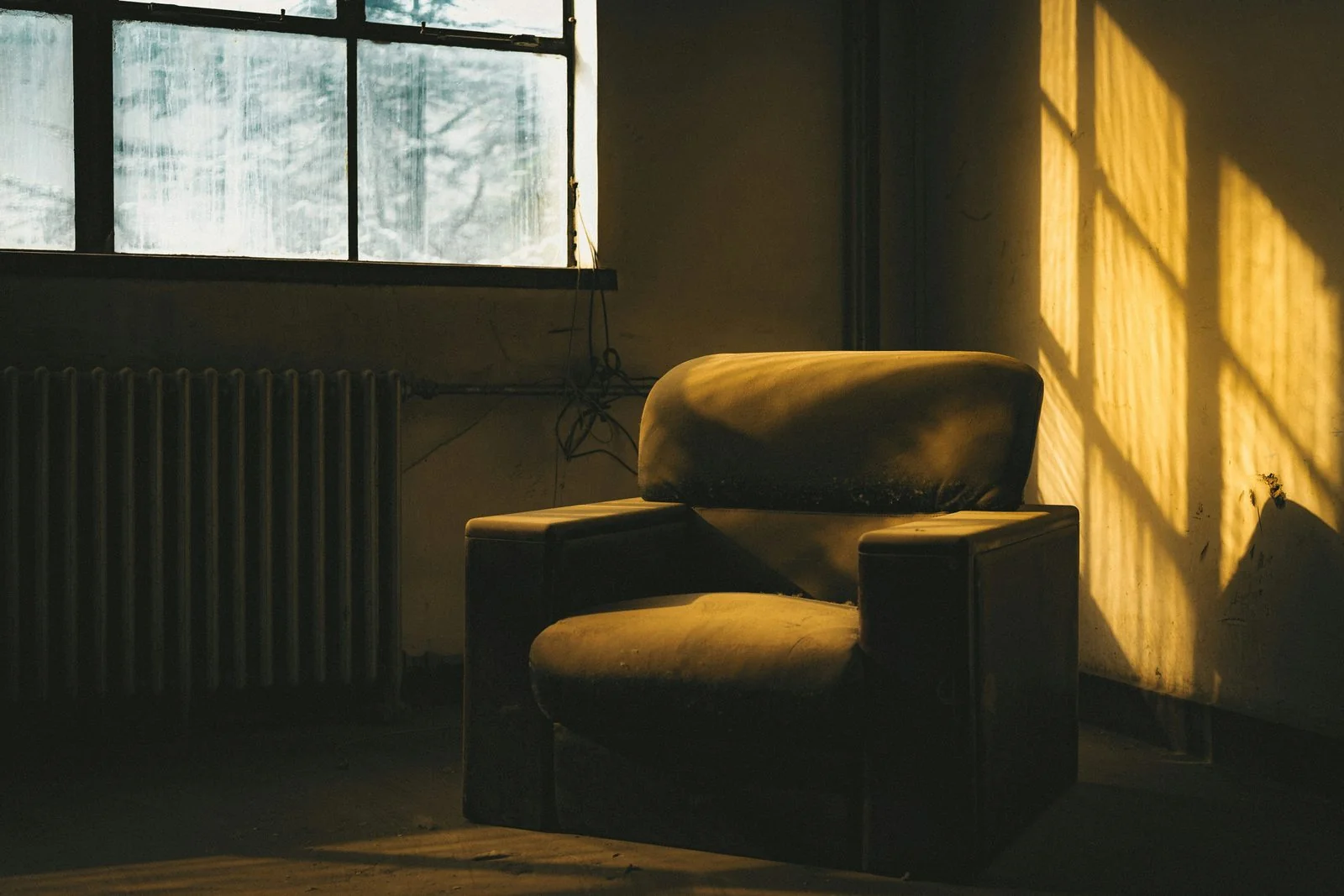 An empty armchair beside a window, lit by warm afternoon light.