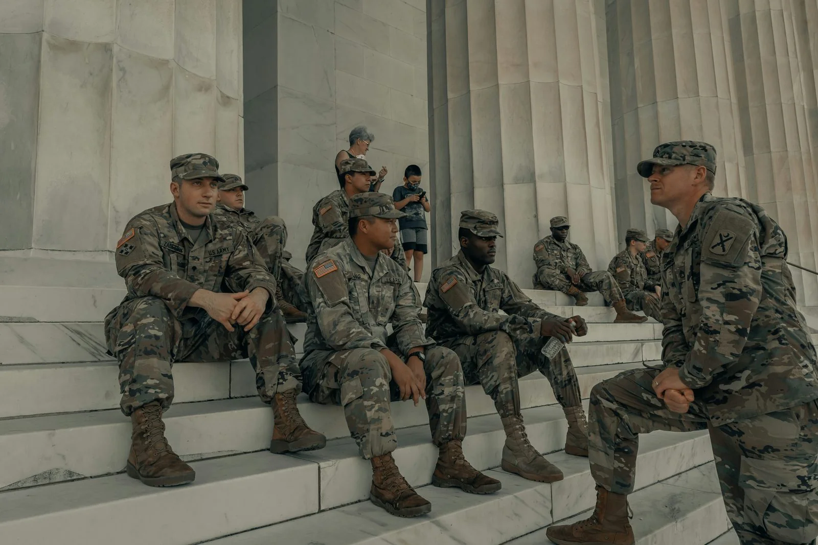 Service members in uniform sitting on stone steps, in conversation.